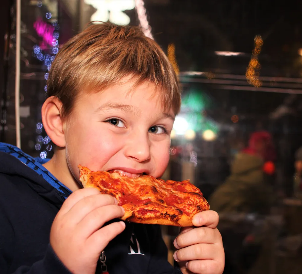 young boy eating a slice of pepperoni pizza
